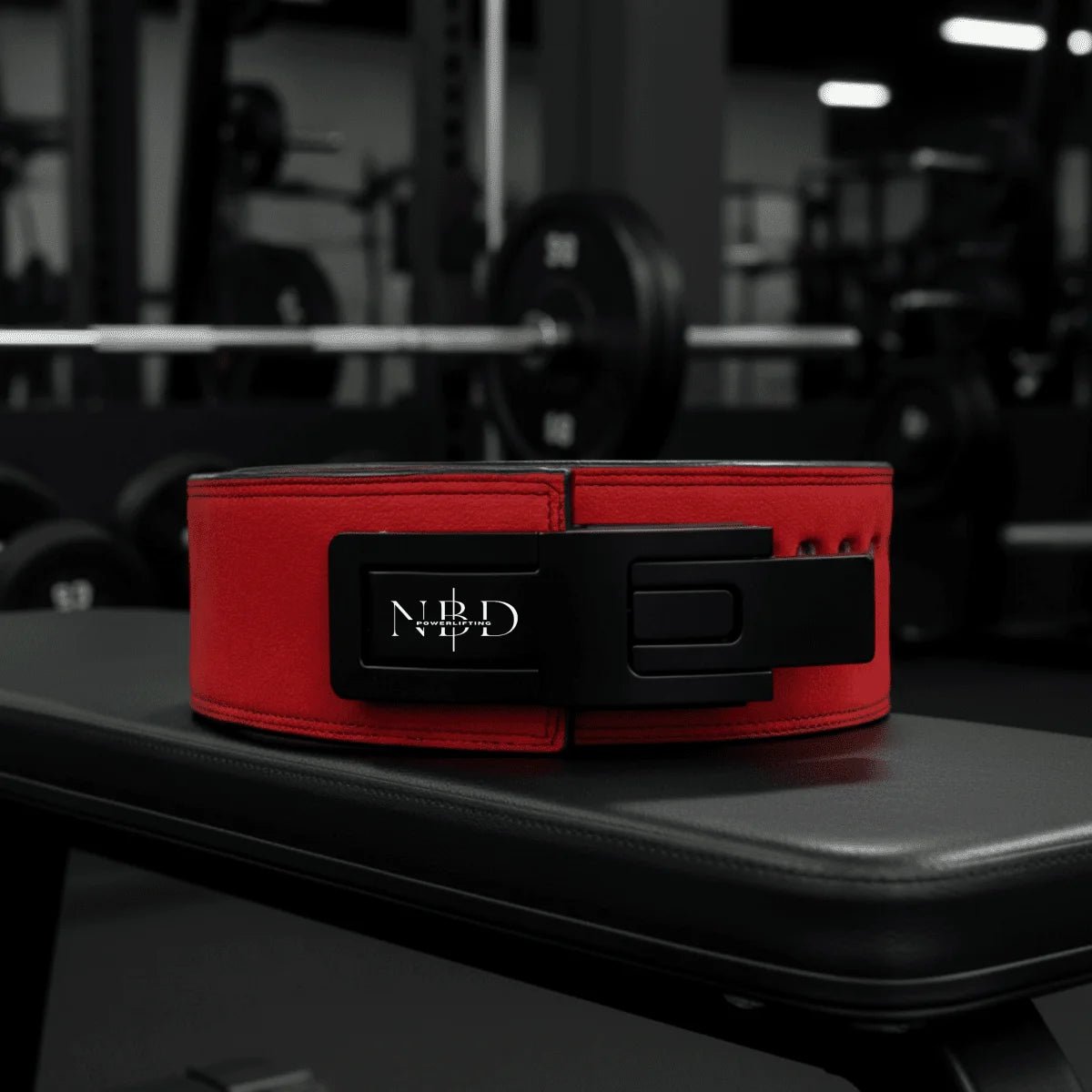 Red weightlifting belt with a brand logo on a black surface in a gym setting