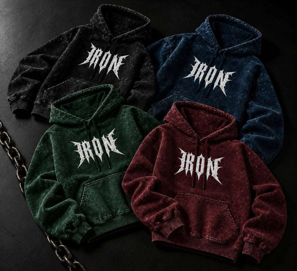 NBD IRON acid wash hoodie in all four colours — black, navy blue, bottle green and maroon laid out on a dark floor beside a steel chain