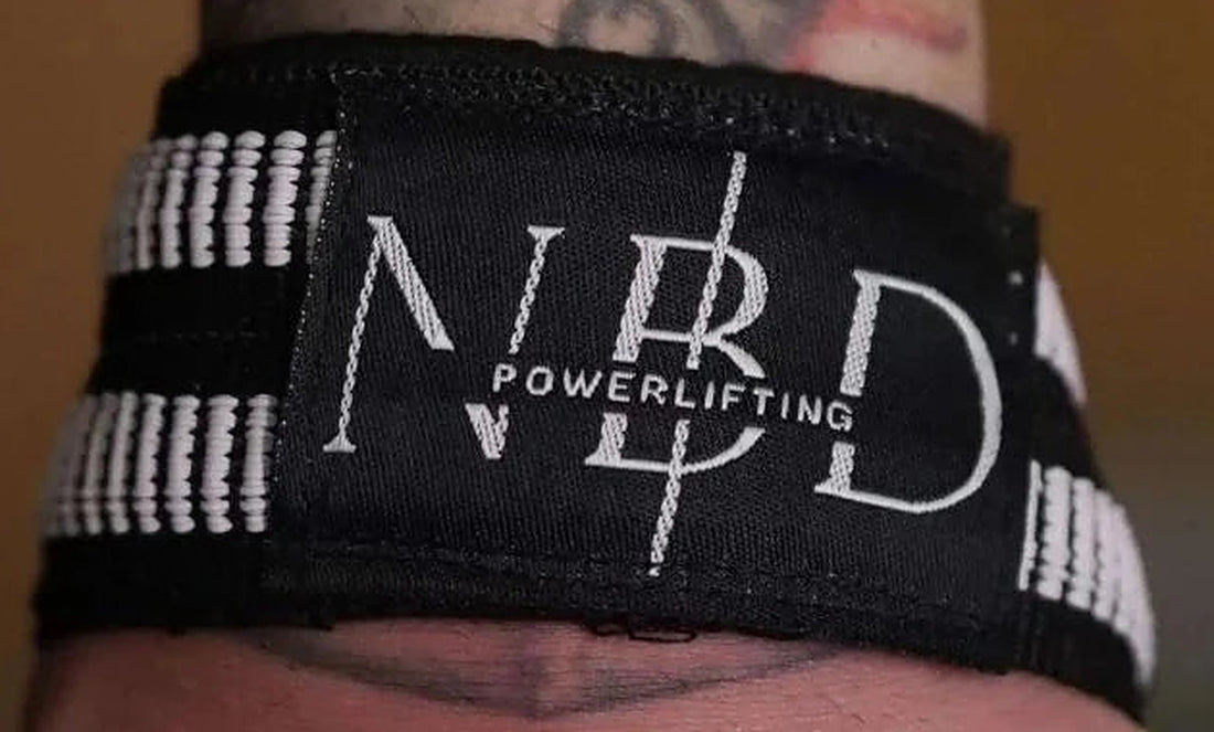 NBD lifting strap worn on the wrist, showing the white rubber ribs and stitched NBD Powerlifting label