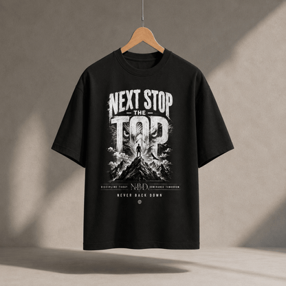 NBD 'Next Stop The Top' oversized T-shirt in black, hanging on a wooden hanger, front print of a lifter on a mountain summit with 'Never Back Down' below